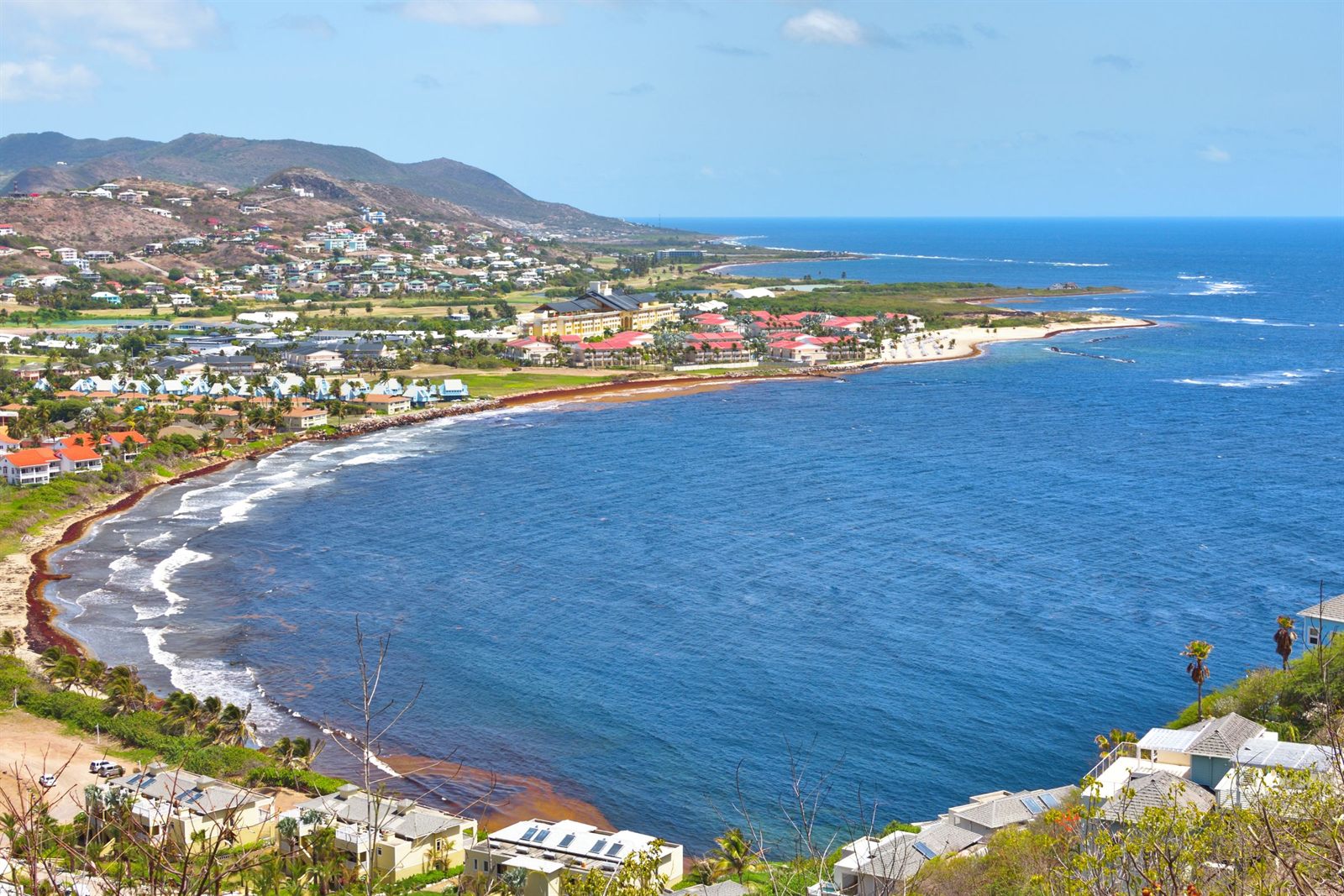 Curving bay and green hills on the coast of St. Kitts under a blue sky
